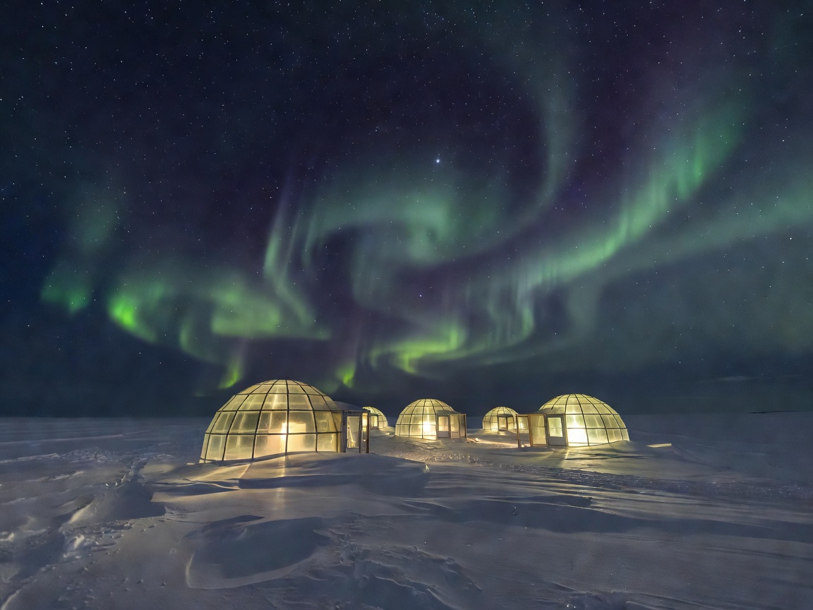 Heated glass igloos lit up against snowy Arctic night sky